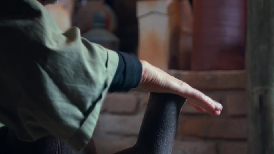 A potter holds a dark clay piece in his hands, with the Cunha studio in the background