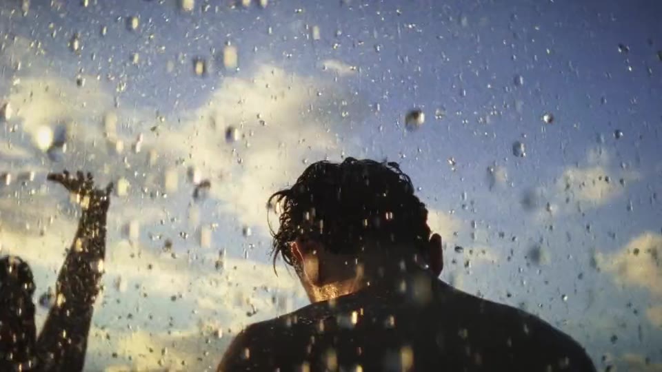 Quatro pessoas caminham por uma estrada de terra entre morros na última luz do dia, frame do clipe Pega